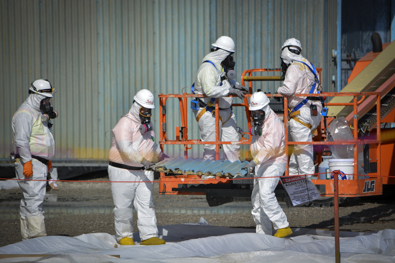 Workers move a transite siding panel from the X-326 Process Building in preparation for wrapping and removal.